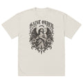 Saint Order Fallen oversized faded-bone tee, front view with winged figure, broken halo, lilies and charcoal botanical artwork.